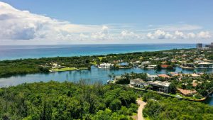 Scenic coastal landscape with lush greenery, calm blue water, and small islands under a clear sky.